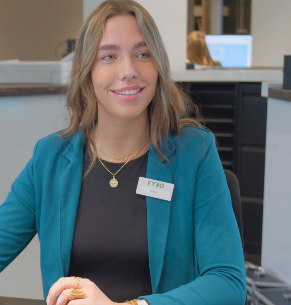 Hilde lacht achter de balie in een turquoise blazer